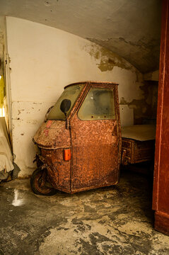 Heavily rusted cab of a Piaggio Ape 50 parked in a backyard driveway; an abandoned Italian three-wheeled commercial vehicle found in a barn&mdash;Gallipoli, Puglia, Italy 25.11.2025