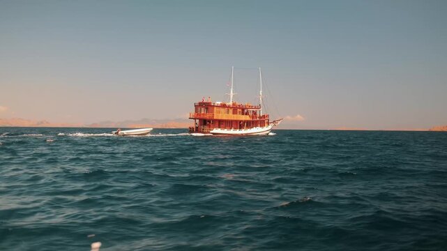 View of a traditional phinisi wooden boat sailing on the blue sea with a small boat in tow near Pulau Sebayur Besar in Komodo, East Nusa Tenggara, Indonesia.