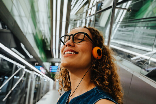 Curly-haired woman enjoys music while commuting in a modern station