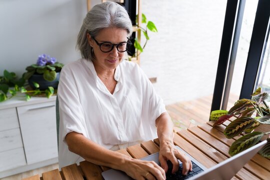 White Woman typing on laptop at wooden desk in home office with plants