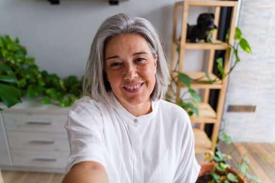 Middle aged white woman smiling and taking selfie indoors with plants