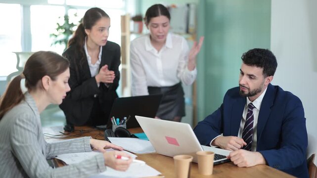 Group of women scold young man while he sits looking sad in office 