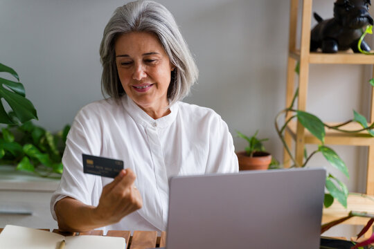 Mature white woman using laptop and payment card for online shopping