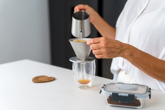 Hand brewing coffee with a metal kettle and filter in a kitchen