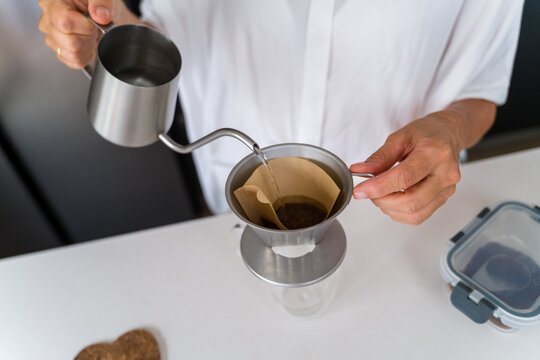 Pouring water for coffee brewing with metal dripper in kitchen