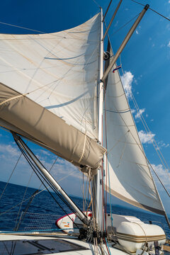 White sails filled with wind against a blue sky above a sailing yacht. Wind powered navigation and freedom at sea.