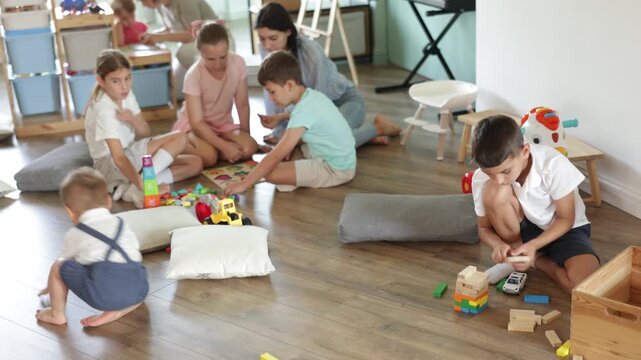 Boy passionate about game with car, children toddler, infant, baby sit on floor and spend playing time in childcare center or daycare in background