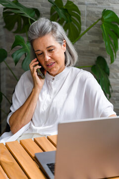 White Woman talking on phone using laptop indoors by plants