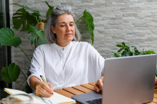 Mature white woman writing and working on laptop
