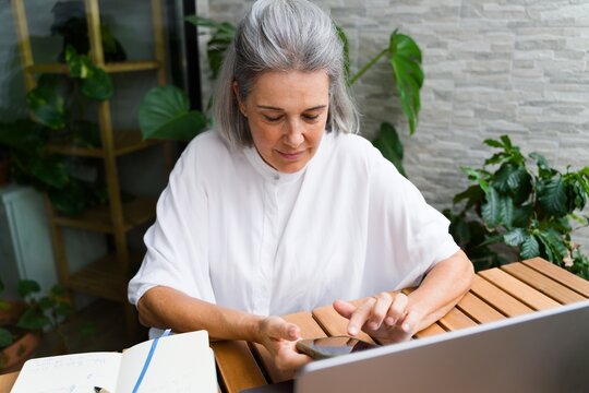White Woman with gray hair using smartphone at wooden table indoors
