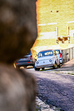 White vintage 1960s Fiat 500 L with a folding roof parked by a historic city wall; a classic Italian cult microcar; Montepulciano, Tuscany, Italy 02.12.2025