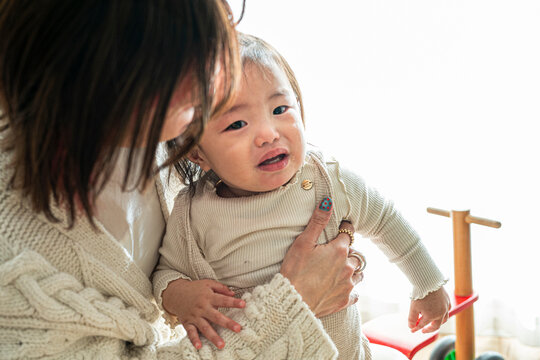 Asian Mother Holding Crying Toddler Girl Comforting Her Softly Indoors