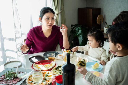 Asian Woman Gesturing while Talking with Family and Kids at Dining Table