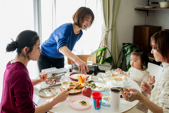 Asian Woman Pouring Wine for Friends at Home Party Lunch Dining Table