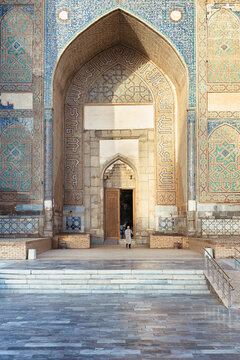 Bibi Khanym Mosque entrance portal with intricate tilework and a lone visitor in Samarkand, Uzbekistan. Monumental Islamic architecture with turquoise and gold mosaic patterns, ideal for travel.