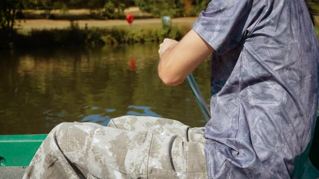 Close up of teenage boy paddling canoe across calm park lake. Hands gripping paddle during active summer water sport. Youth fitness, outdoor recreation and healthy lifestyle in nature