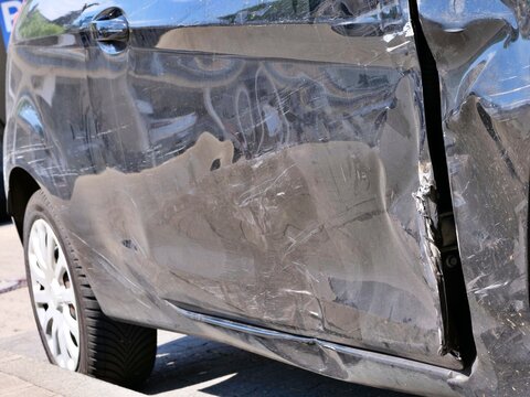 Side view of a heavily dented black car body panel with deep scratches and bent door frame following a side-impact collision.