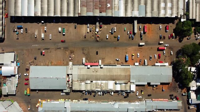 Aerial view of bustling industrial warehouse complex with numerous cars and trucks parked and moving between buildings.