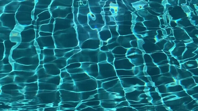 Blue swimming pool water surface showing bright sunlight reflections and ripple patterns.