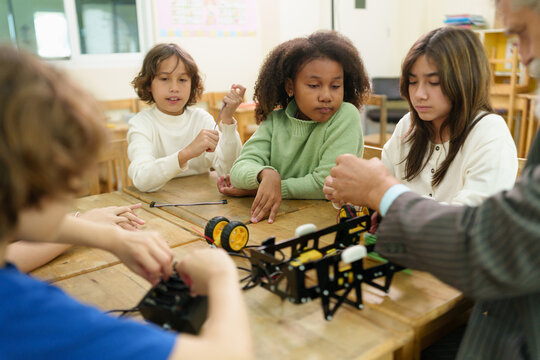 Diverse children work together on a robotics project with teacher guidance in a classroom, exploring STEM education, engineering, technology, teamwork, problem solving and creative learning.