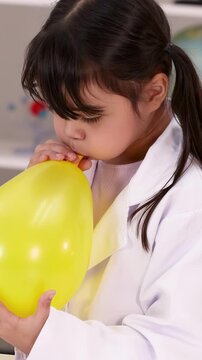 Young Girl in Lab Coat Blowing Up Yellow Balloon for Science Experiment