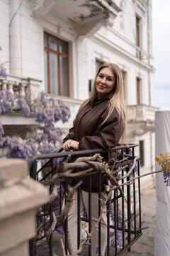 Historic villa porch featuring a blonde woman standing amidst blooming wisteria flowers for travel lifestyle project