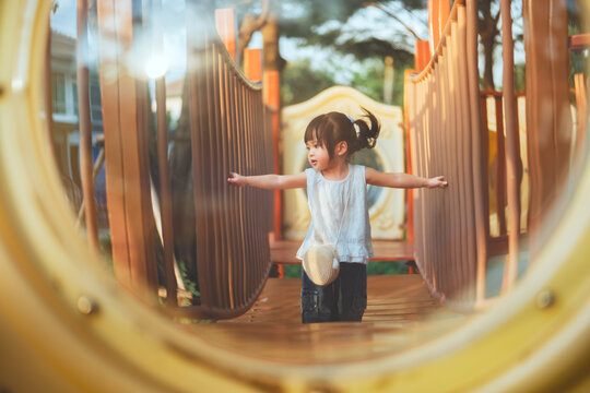 Playful toddler girl walking with arms outstretched for balance on playground bridge outdoors, active childhood play, physical development, coordination, movement, fun and early motor skills