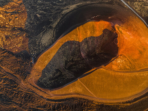 Aerial view of the volcanic crater of Mount Etna with vibrant orange and dark black lava flows across the rugged terrain in Catania, Sicily, Italy.