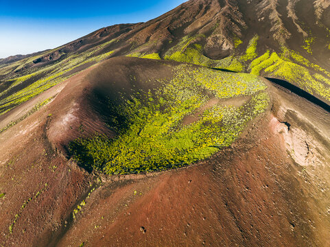 Aerial view of Etna volcanic crater with vibrant green vegetation and dark volcanic soil under a clear blue sky Catania, Sicily, Italy.