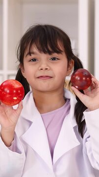 Young Girl in Lab Coat Holding Red Apples in Science Classroom