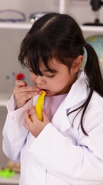 Elementary Student in Lab Coat Deflating Yellow Balloon in Science Classroom