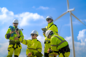 Fototapeta premium Bearded technician holds a grey inspection drone in both hands while a kneeling colleague reaches toward its rotor and a huge white turbine rises in the background