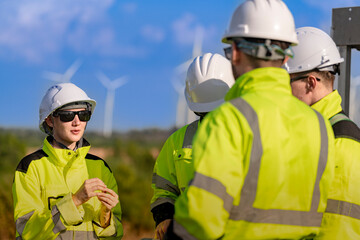 Fototapeta premium Female wind technician smiles mid sentence while briefing colleagues outdoors, her white hard hat and dark sunglasses lit by the low late afternoon sun in bright tropical sun