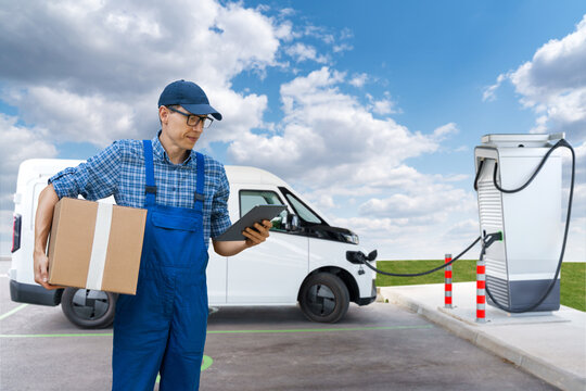 A man with a digital tablet stands next to electric delivery van	