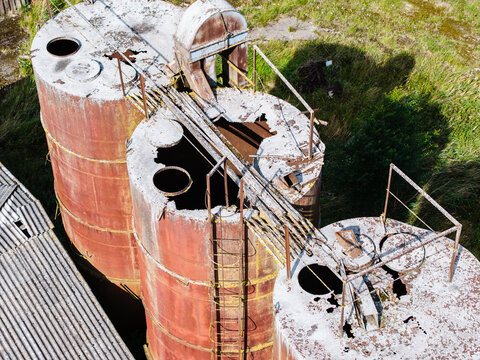 Aerial view of abandoned and rusted Soviet-era agricultural silos showing structural decay and weathered metal surfaces in Kulciems, Talsi Municipality, Latvia.