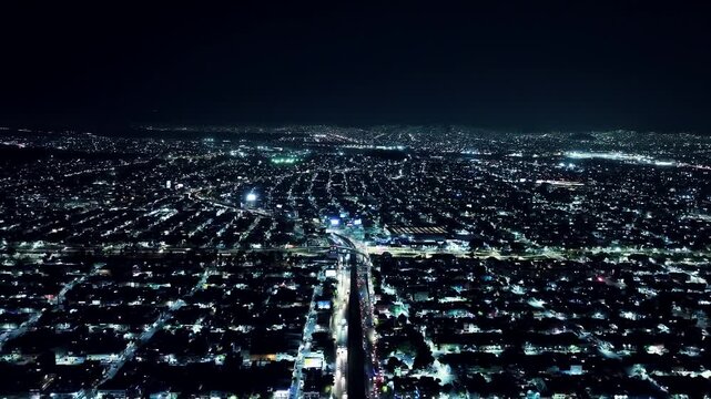 Aerial drone perspective of glowing city traffic at night showing urban sprawl and illuminated residential streets.