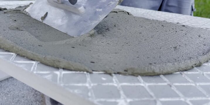 Worker applying wet concrete with a trowel on a textured surface, showing the smooth transition of material across the workspace in a construction setting