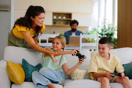 Parents dealing with screen time addiction, gaming, and technology, as mother attempts to limit children's digital entertainment while father works on laptop in the background