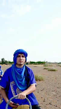 Marrakech, morocco. August 9, 2026. Caucasian tourist wearing a blue tuareg djellaba and turban while riding a dromedary camel during an excursion in the marrakech desert