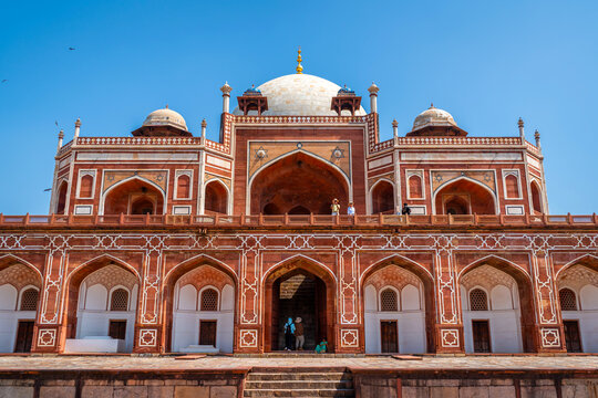 Symmetrical view of the grand red sandstone mausoleum with white marble dome and intricate arches under a bright blue sky at Humayun's Tomb, Delhi, India.