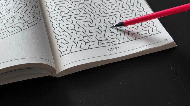 Red pencil resting on an open puzzle book with a printed maze. Close-up of a labyrinth game representing brain training, problem solving, concentration, logical thinking and relaxing screen-free leisu