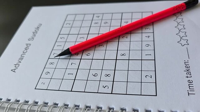 Vertical close-up of a red pencil pointing at a sudoku puzzle in a spiral notebook. Number game representing logical thinking, concentration, problem solving, brain exercise and an educational leisure