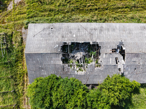 Aerial view of a collapsed and abandoned Soviet-era agricultural building with a large hole in the roof, surrounded by overgrown vegetation in Kulciems, Talsi Municipality, Latvia.