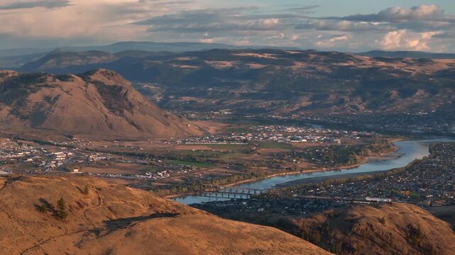 Panoramic view of kamloops valley at golden hour with river and highway bridge.