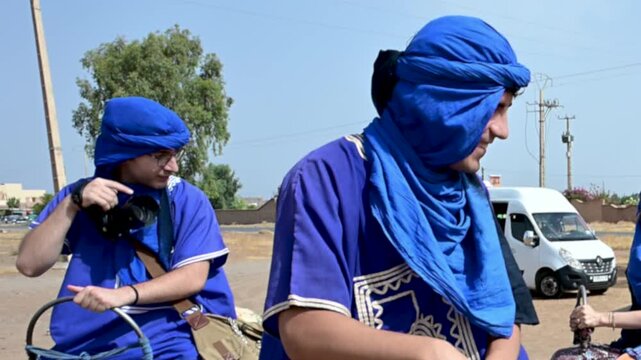 Marrakech, morocco. August 9, 2026. Berber guides wearing traditional blue tagelmust turbans leading a camel tour. Tourists enjoying a dromedary ride safari in the agafay desert