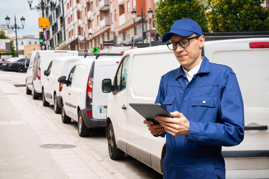 Fleet manager with digital tablet supervising rows of white delivery vans	