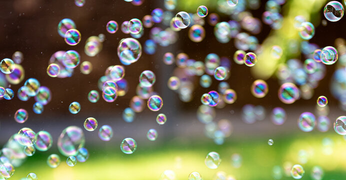 Rainbow soap bubbles floating outdoors. Bright summer background with green grass.