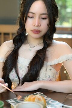 Young woman with long dark hair sitting at table with dessert in cozy cafe setting