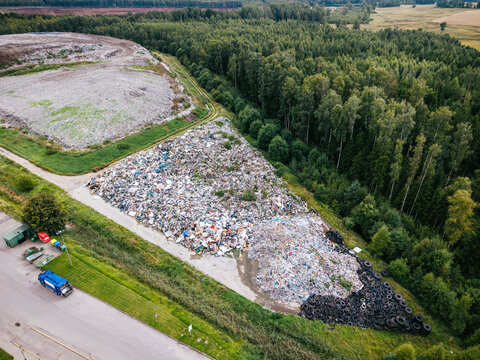 Aerial view of a municipal solid waste landfill with piles of sorted trash, discarded tires, and processing equipment near a forest in Laidzes pagasts, Talsu novads, Latvia.