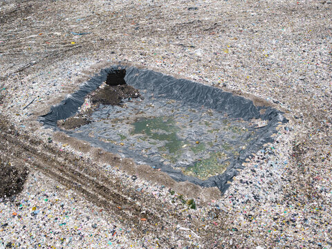 Aerial view of a municipal solid waste landfill with a lined pit containing water, surrounded by processed waste materials in Laidzes pagasts, Talsu novads, Latvia.